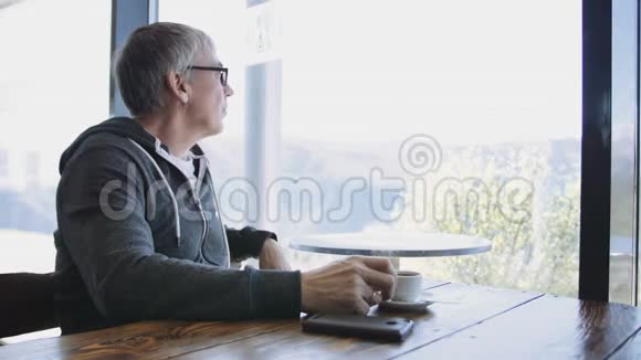 白种人高级运动风格的男人看着窗外的咖啡馆一个年老的灰色男人在桌旁喝咖啡视频的预览图
