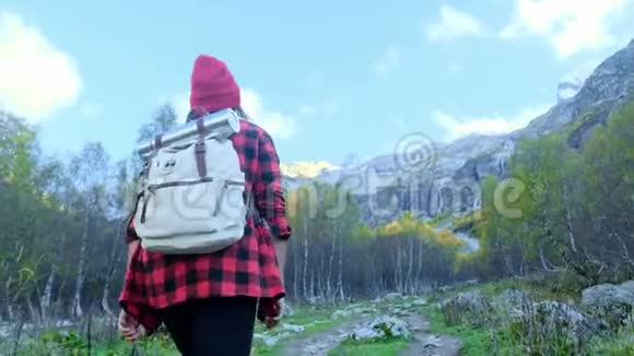 活跃的年轻时髦女孩穿过树林沿着山间的小路走她戴着一顶红帽子视频的预览图