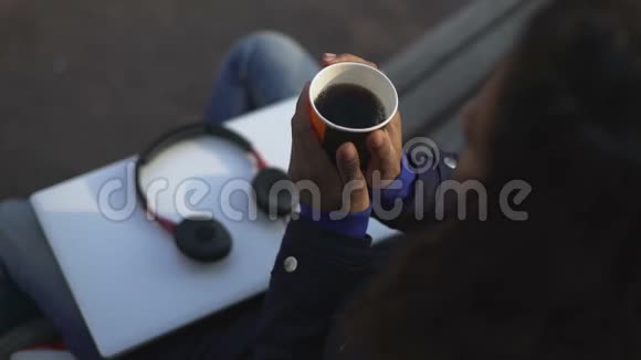 女人温暖双手在户外坐着的时候拿着一杯香喷喷的热饮视频的预览图