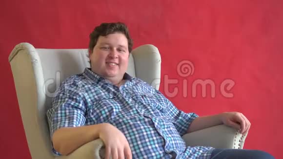 快乐的年轻胖子坐在扶手椅上微笑着看着镜头视频的预览图