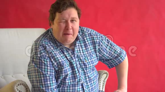 身着格子衬衫的快乐胖子的肖像在红色背景下对镜头戏谑地眨眼视频的预览图
