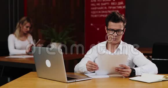 年轻的商人戴着眼镜手提电脑和纸在办公室工作商务人事文书工作视频的预览图