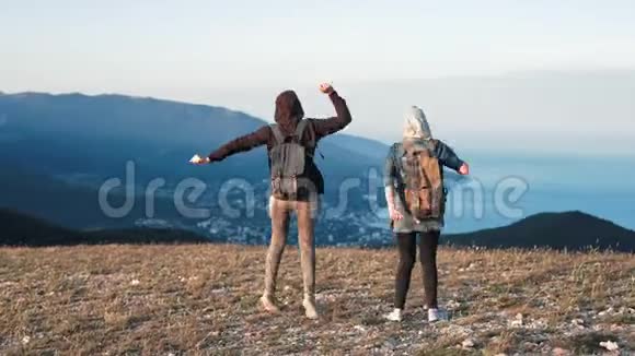 两个年轻快乐的女人在美丽的山顶上跳舞举起手臂越过夕阳的天空视频的预览图