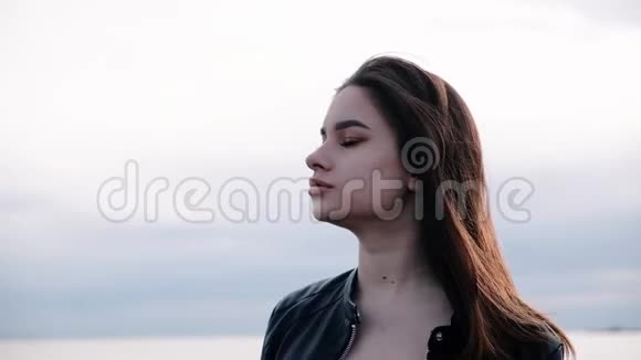 美丽的年轻女孩黑发在海边日落的光慢动作视频的预览图