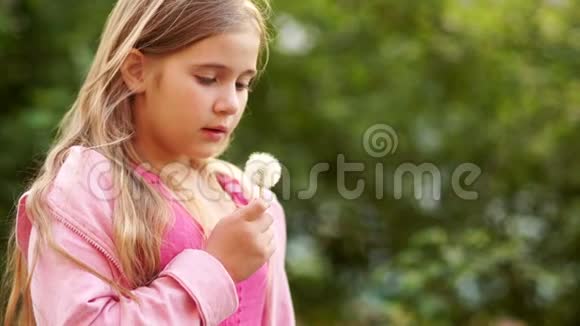 一个留着长发的可爱女孩把蒲公英的种子吹下来它们在夕阳的光线下在风中飞翔夏季视频的预览图