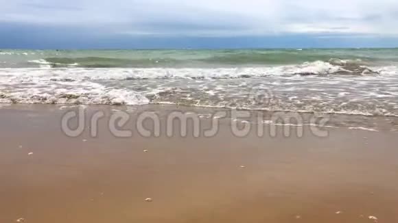一个人沿着海岸线走沙滩上有海浪和海沫视频的预览图