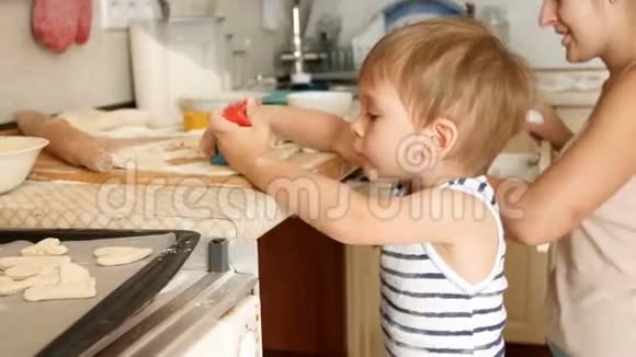 可爱的学步男孩帮他妈妈做饭和在厨房做面团的4K镜头视频的预览图