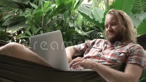 男人用笔记本电脑躺在吊床上微笑视频的预览图