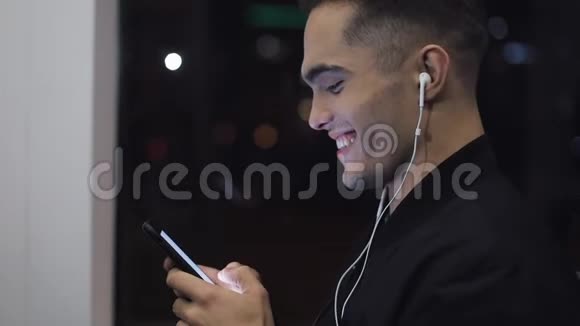 戴着耳机听音乐和在公共交通工具上浏览手机的年轻头男的肖像城市视频的预览图