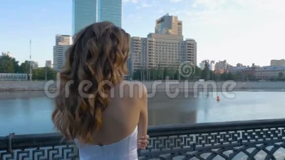 美丽的年轻女孩长发穿着白色的裙子站在城市的海滨视频的预览图