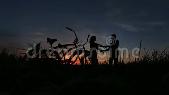 喜欢骑自行车散步这对敏感的情侣在红灰色天空的田野上跳舞的剪影视频的预览图