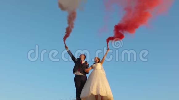 幸福的新娘和新郎在蓝天上挥舞着粉红色的烟笑着蜜月浪漫两者之间的关系视频的预览图