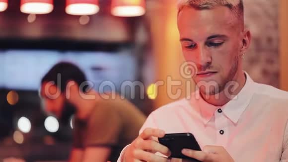 年轻英俊的男人在夜间咖啡馆里拨打电话并在智能手机上交谈他坐在霓虹灯旁边视频的预览图