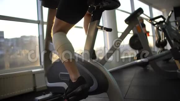运动员男性带绷带腿早上骑固定自行车康复视频的预览图