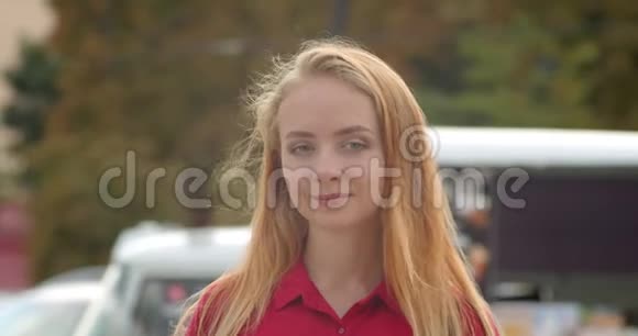 年轻美丽的白种人女性穿着红色的裙子看着站在城市户外的摄像机视频的预览图