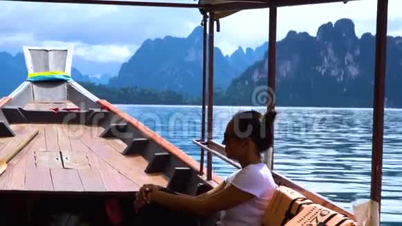 亚洲女孩乘长尾船在群山之间的湖上航行视频的预览图
