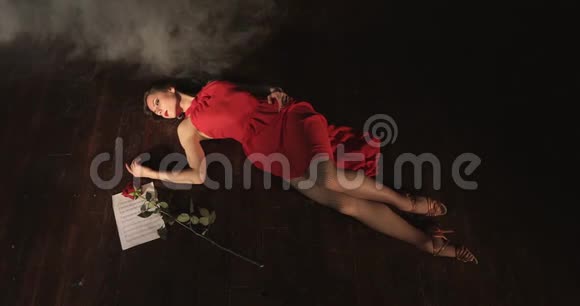 一个身材苗条的年轻女子穿着红色连衣裙在表演探戈后躺在烟雾中视频的预览图