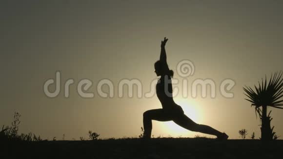 活动女性练习瑜伽姿势日落时做练习的剪影视频的预览图