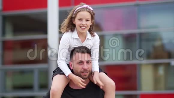 父女家庭幸福女孩坐在男人的肩膀上欢快地笑着张开双臂视频的预览图