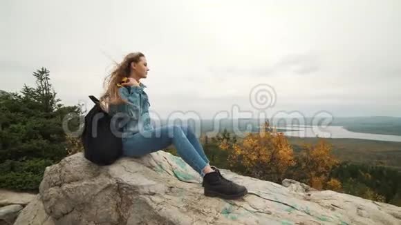 一个年轻的女人坐在山顶上看着美丽的风景想着生活一个女孩视频的预览图