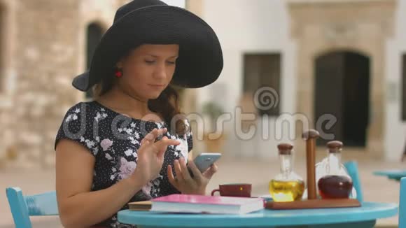漂亮的女孩坐在街边的咖啡馆里在智能手机上打字聊天视频的预览图