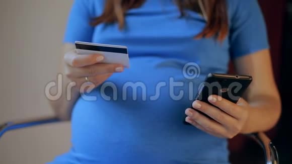 持有信用卡并使用手机进行网上购物的孕妇视频的预览图