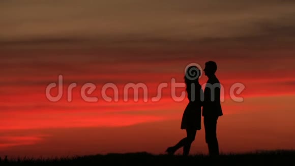 这对夫妇在日落时在红天上轻轻亲吻的剪影浪漫的气氛视频的预览图