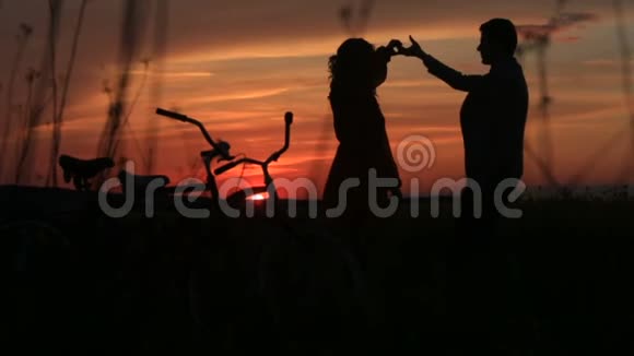 敏感的情侣在红艳艳的夕阳下在田野上跳舞剪影的完整视角步行视频的预览图