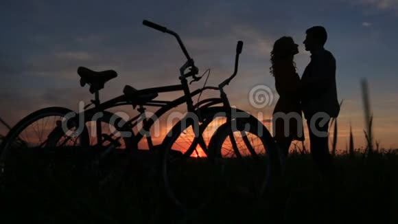 在红灰相间的夕阳下这对相爱的夫妇在田野里温柔地接吻骑自行车走路视频的预览图