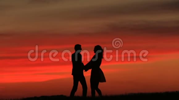 美丽的幸福夫妇的剪影轻轻地亲吻着红色的夕阳视频的预览图