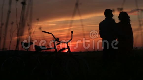 在田野的夕阳下这对温柔相爱的夫妇的剪影轻轻地亲吻着红色明亮的天空散步与散步视频的预览图