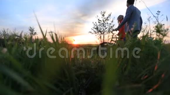 这对微笑的幸福夫妇正骑着自行车沿着美丽的盛开的田野在明亮的五颜六色的日落中散步视频的预览图
