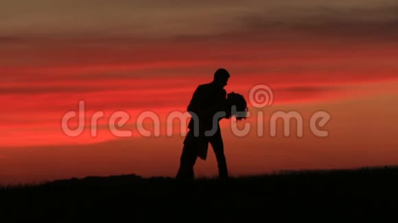 这对可爱的夫妇在日落时在红天上跳舞时温柔地接吻的剪影视频的预览图