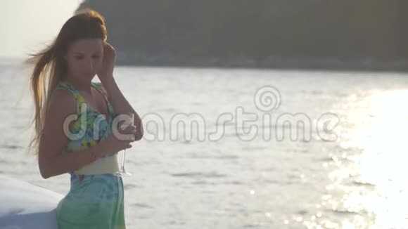 一个平静的女孩拿着一杯香槟在日落时漂浮在游艇上视频的预览图