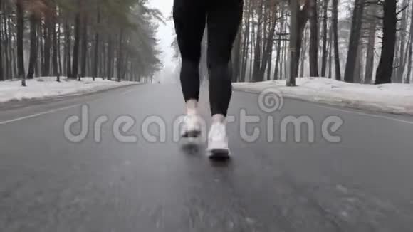 年轻迷人的白种人女孩在冬天带着耳机在雪地公园跑步关闭后跟镜头视频的预览图