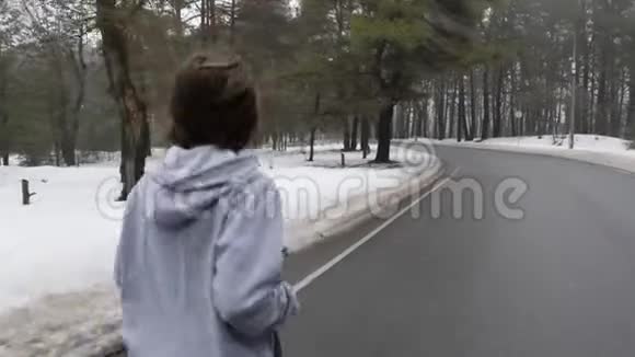 年轻迷人的白种人女孩在冬天带着耳机在雪地公园跑步关闭后跟镜头视频的预览图