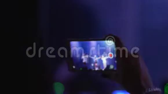 观众在灯光照明的背景下在夜间娱乐的智能手机上制作视频视频的预览图