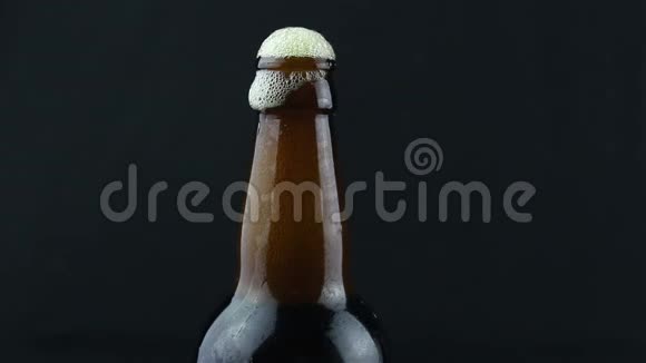 啤酒泡沫沿着一瓶雾蒙蒙的啤酒流下来啤酒泡沫顺着一瓶深色啤酒流下来视频的预览图