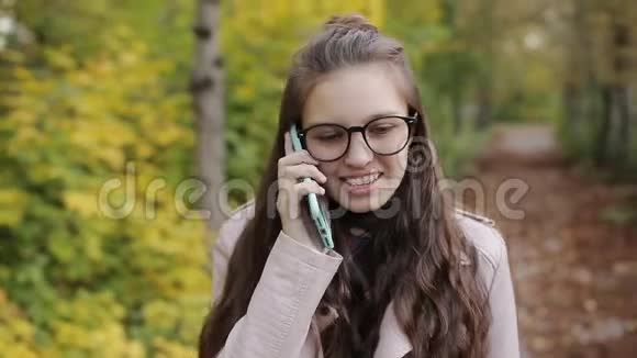 少女在公园里散步在手机智能手机上聊天秋天的天气黄叶和凉爽视频的预览图