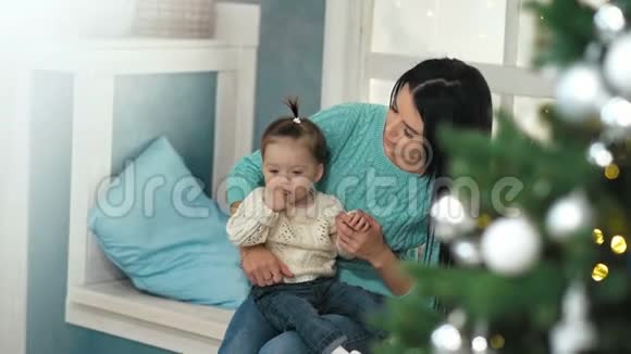 母亲抱着坐在圣诞树旁窗台上的女儿视频的预览图