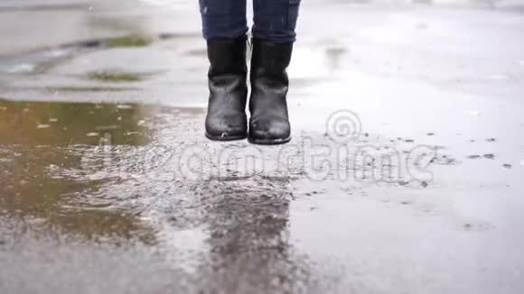 一个穿着黑色皮靴的女孩在雨中在秋天的水坑里跌倒视频的预览图