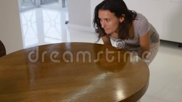 一个穿着紧身灰色T恤领口很深的女人用抹布擦拭一张大餐桌视频的预览图