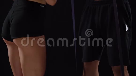 男女运动员在演播室里用黑色背景的弹性带在二头肌上做运动视频的预览图
