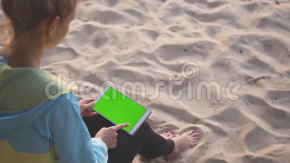 一个女孩坐在沙子上用一个带有色度键屏幕的平板电脑扫荡视频的预览图