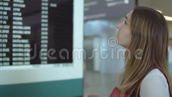 漂亮的年轻女性站在记分板附近有通知和选择号码飞行视频的预览图