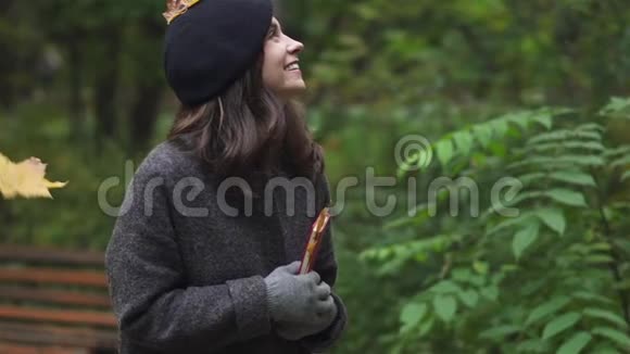 快乐的黑发女人带着书在树叶下微笑视频的预览图