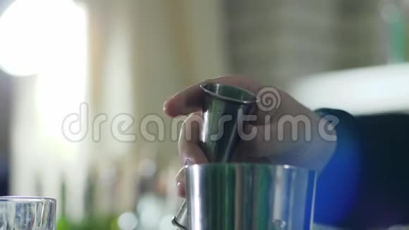 人的手握着跳汰机在没有聚焦的背景上缓慢地将液体倒入金属杯中视频的预览图