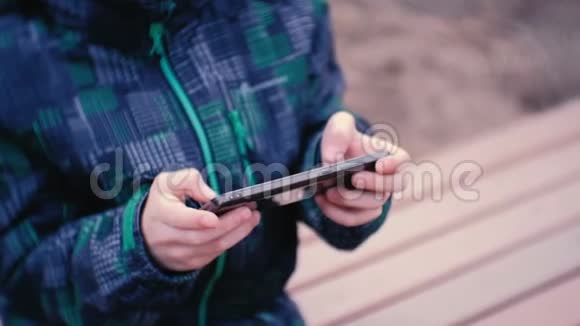 男孩坐在公园里的长凳上用手机玩游戏特写男孩手视频的预览图