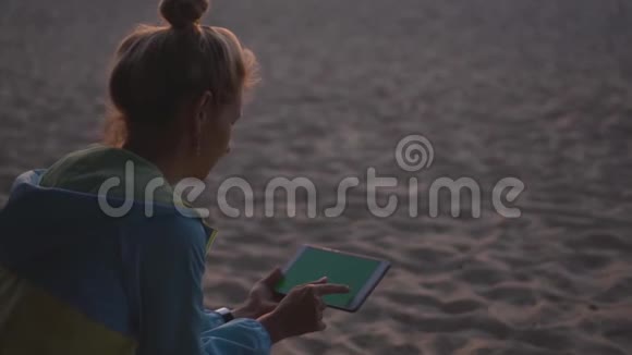 在日落时分一个使用平板电脑坐在海滩上的女孩铬化视频的预览图