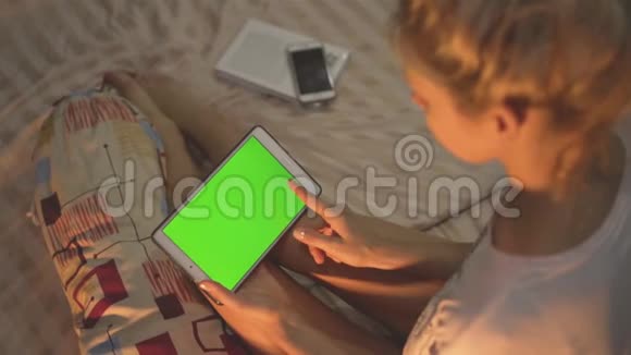 一个女孩坐在床上使用带有色度键屏幕的平板电脑扫荡视频的预览图